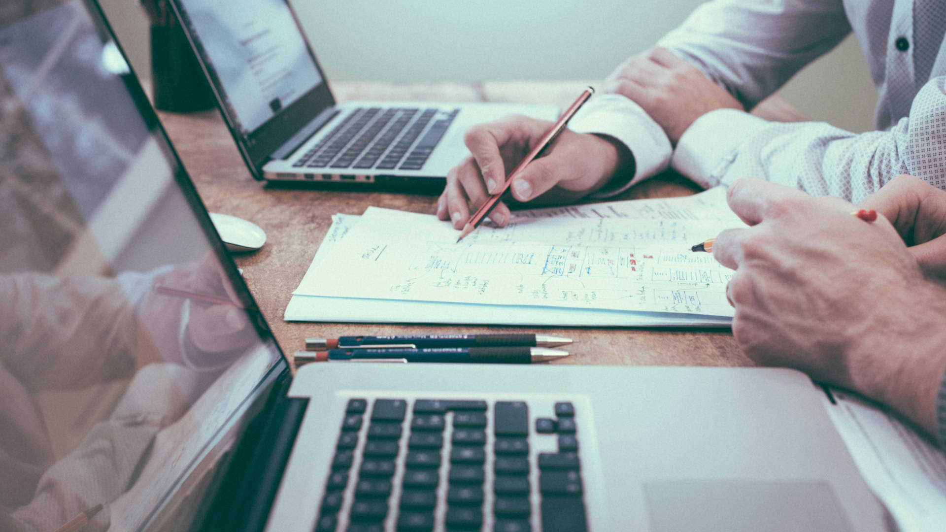 Two people using computers while taking notes
