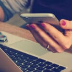 A person on their laptop holding their phone